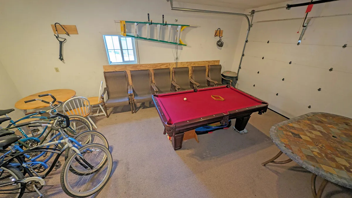 This image showcases a dynamic garage game room featuring a pool table as the centerpiece, bicycles positioned along the wall, and a cozy seating area with a table. The space is brightly lit, evoking a playful and inviting atmosphere where guests can enjoy friendly competitions or relax after outdoor adventures.