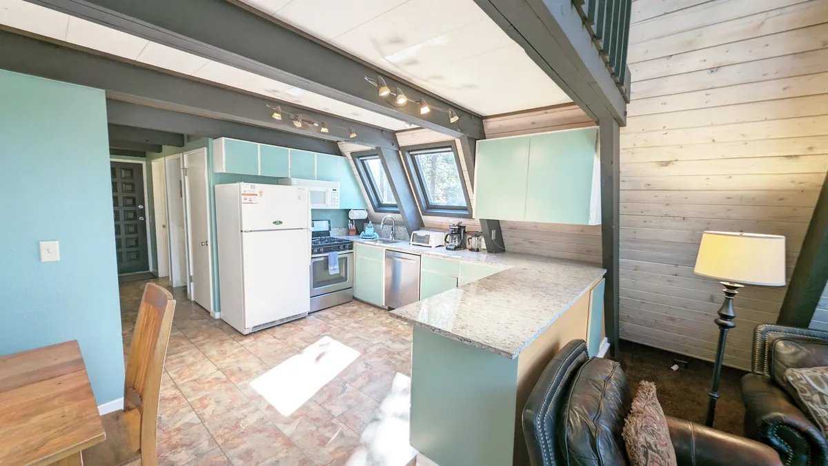This image captures the heart of Trapper 11's communal spaces, featuring a spacious kitchen island, a dining table filled with natural light from large windows, and comfortable seating. The scene radiates warmth and hospitality, showcasing areas perfect for family meals, cooking together, and entertaining.