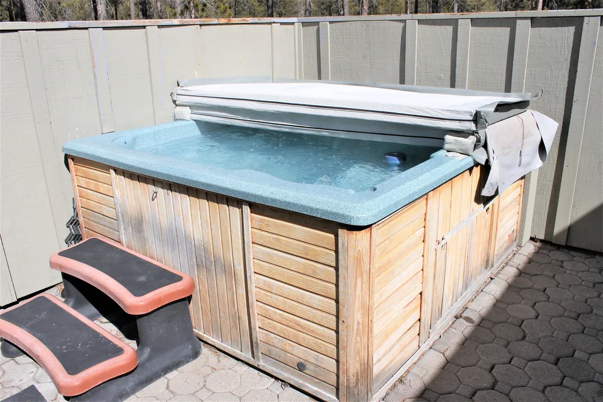 This exterior image captures the private jacuzzi hot tub nestled within a fenced outdoor area, with steps leading up and subtle landscaping around. The setting is tranquil and inviting, perfect for relaxing after a day of adventure at Sunriver, especially under a starry sky as mentioned in the section.