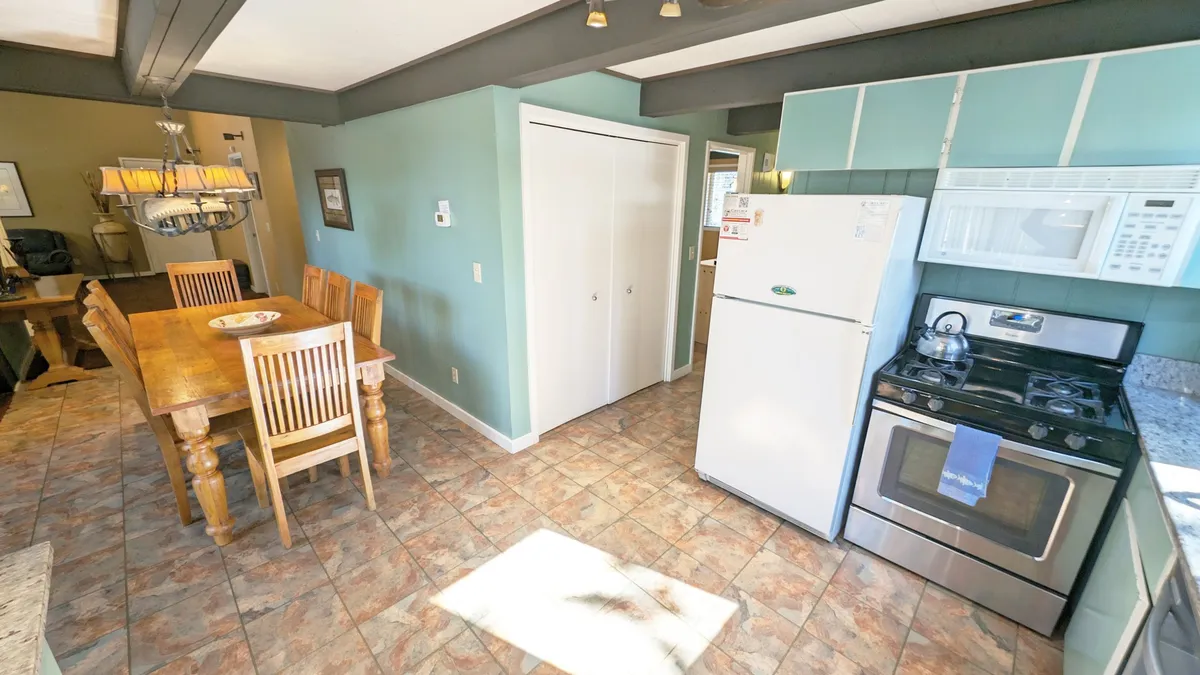 A cozy dining table is surrounded by kitchen appliances and colorful walls, suggesting a warm and lively atmosphere perfect for group meals or celebrations. The view hints at the seamless connection between cooking, dining, and socializing.