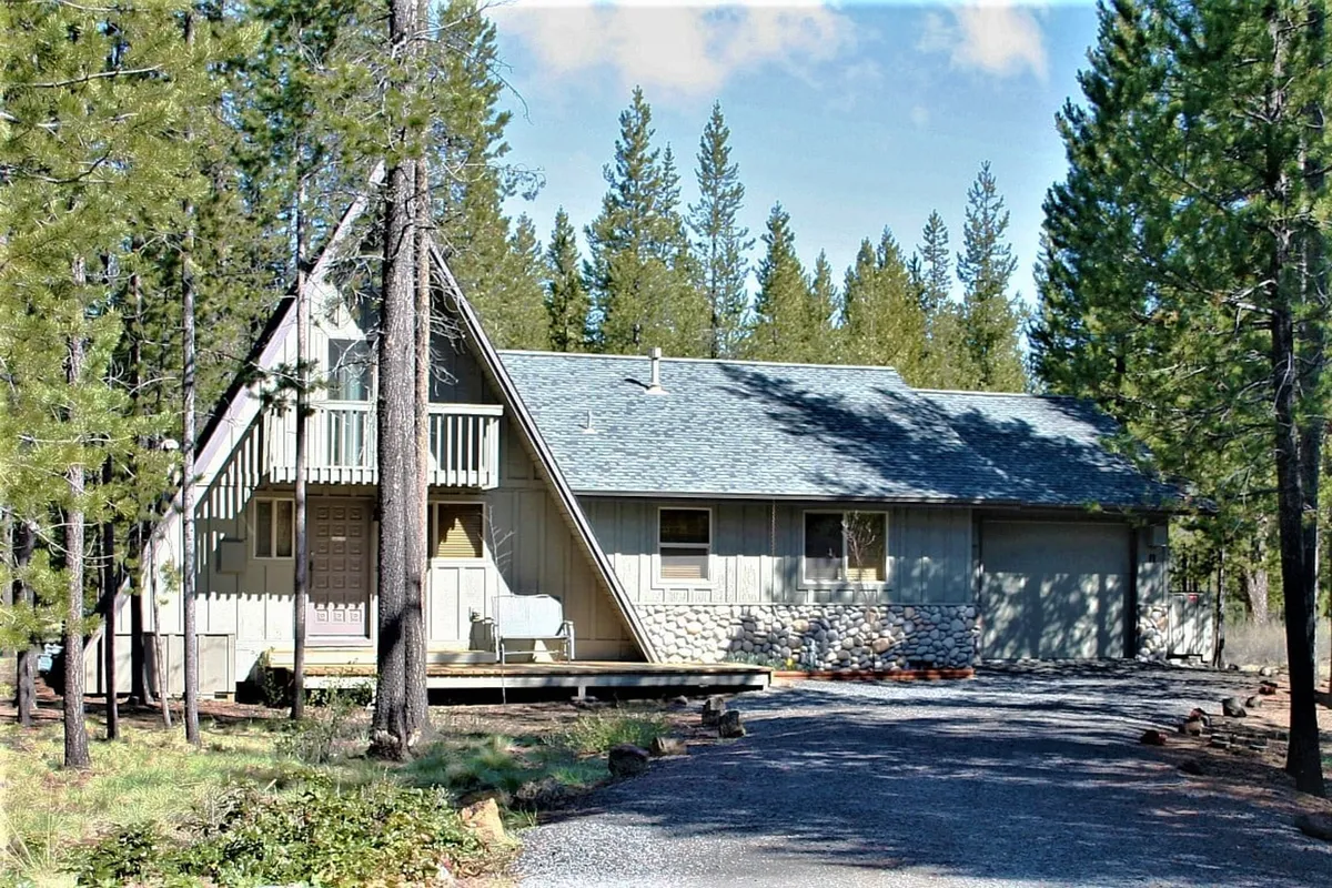 Another exterior view showcasing the home's triangular roofline, welcoming stone facade, wooden porch, and the lush forest backdrop. The porch area hints at opportunities for morning coffee, evening relaxation, and gathering before heading out to local attractions.