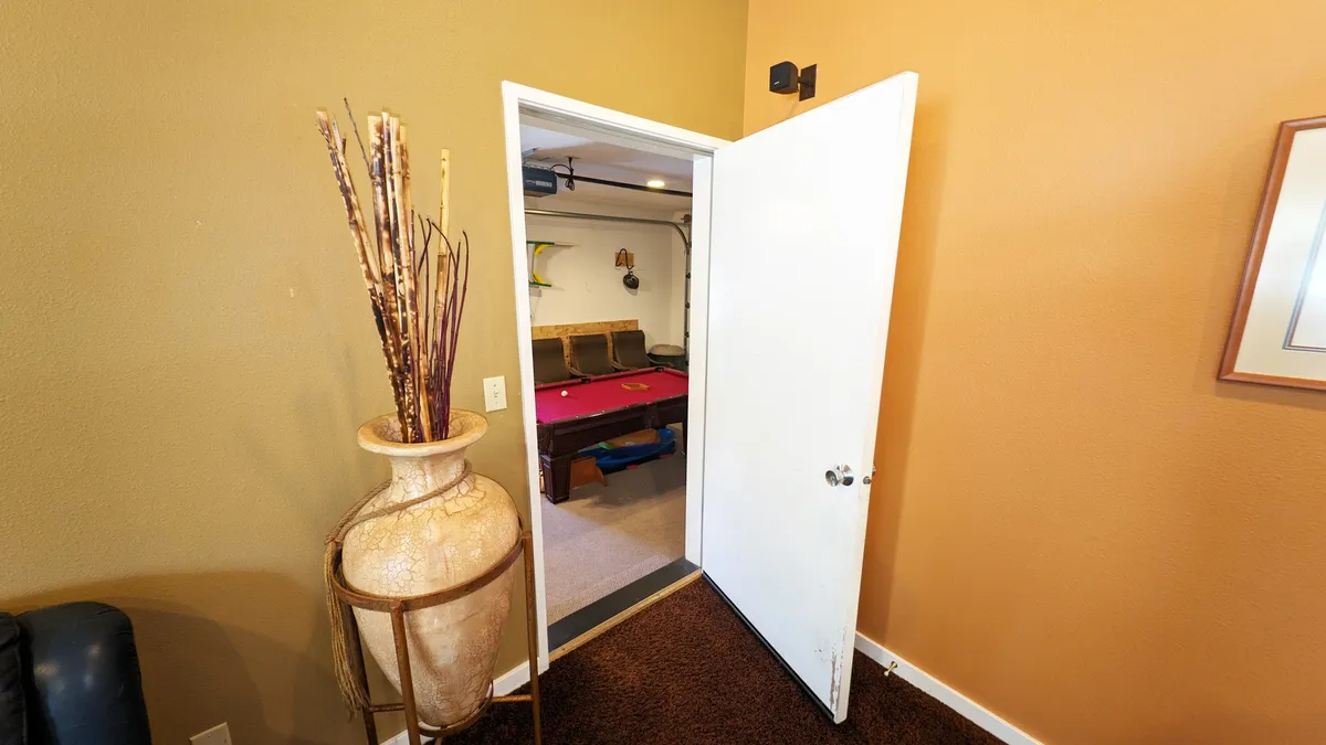 This image offers a welcoming view through an open door into the game room, with a pool table visible in the background. A large decorative vase with dried plants adds a stylish touch, and the open doorway invites guests into the entertainment space.